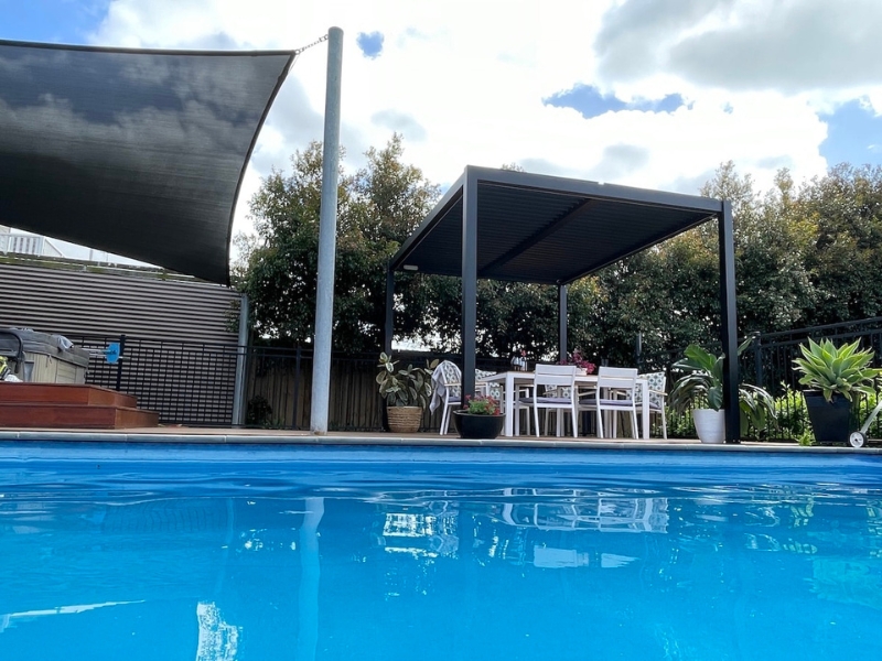 Louvered roof for pergola by the poolside, offering shade and a comfortable outdoor dining space.