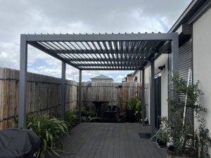 Compact backyard pergola with standard height and louvered roof, surrounded by greenery and modern fencing.