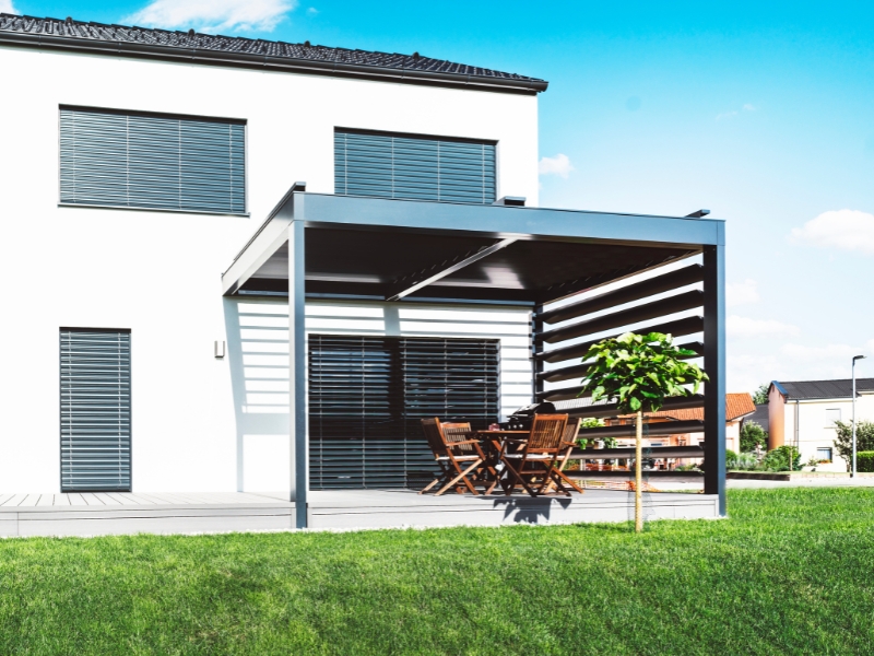 Minimalist pergola with standard height and wooden slats, offering shade for a dining setup in a backyard.