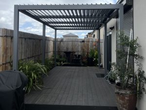 Stylish pergola decking ideas featuring a grey aluminium pergola with louvered roof, dark composite decking, and a private garden setup.