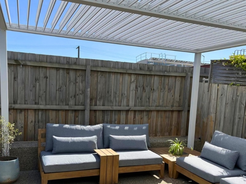 Upgrade your pergola kit by adding white louvered roofing above outdoor lounge seating.
