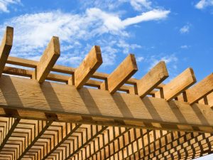 Wooden adjustable pergola top slats against a blue sky.
