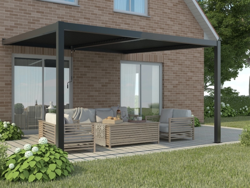 Adjustable pergola with black louvered roof shading an outdoor lounge area beside a brick house.