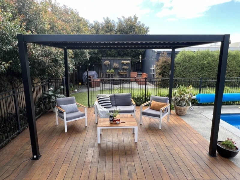 Backyard aluminium pergola with lounge furniture and timber decking beside a swimming pool