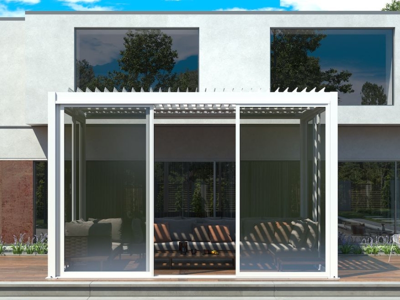 Stylish white pergola area with glass sliding doors and louvred roof beside a modern building.