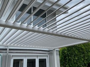 White pergola with adjustable roof above modern patio and French doors