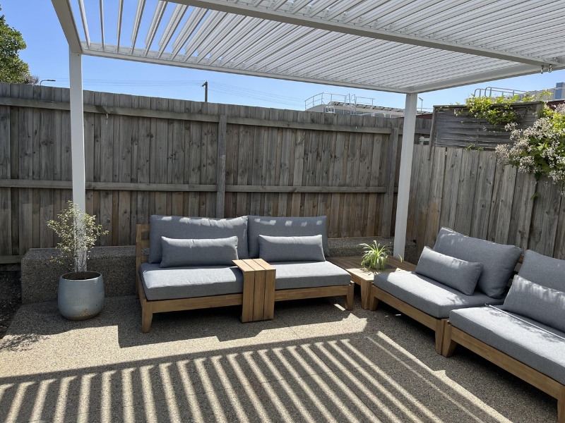 White wall pergola kits covering outdoor lounge with timber furniture and cushions.