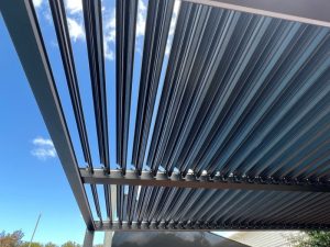 Modern black pergola with adjustable roof open to blue sky in residential outdoor space