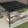 Black portable pergola kits covering timber lounge furniture on a tiled patio beside a brick house