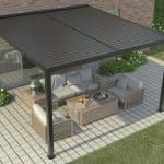 Wall mounted manual louvered pergola in black, attached to brick home with outdoor lounge setting on paved patio.