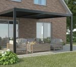 Contemporary patio setup under a black-framed wall-mounted louvered pergola, showcasing minimalist wooden lounge furniture and a red brick house exterior.