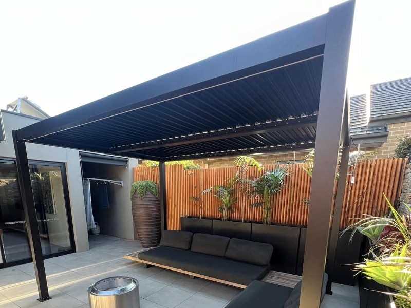 Pergola design plans featuring black louvre pergola over tiled patio with outdoor seating.