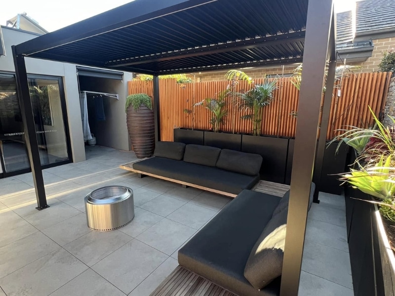 Pergola designs and plans featuring black louvre roof over outdoor lounge with timber privacy screen.