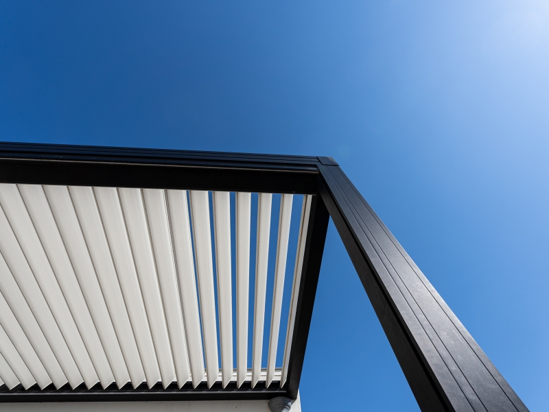 Close-up view of aluminium frame pergola with adjustable white louver roof against clear blue sky