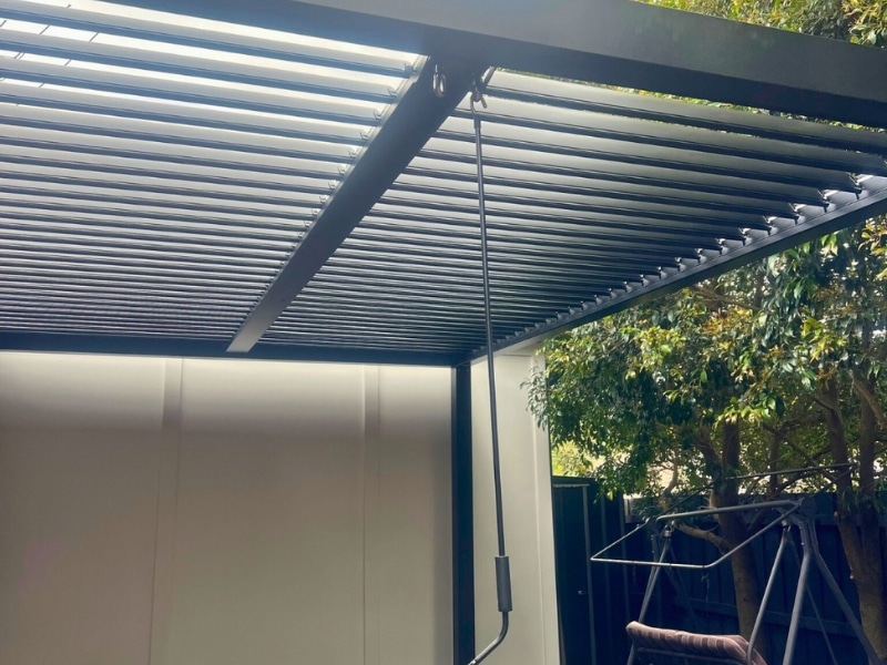 Pergola designs and plans showing black louvre roof installed in shaded backyard area.