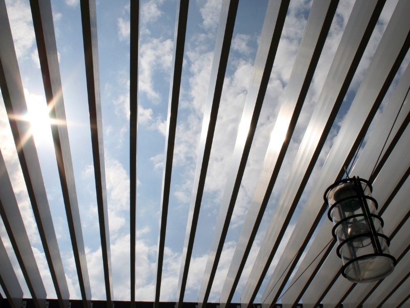 Sunlight filtering through adjustable louvre roof of metal garden pergolas.