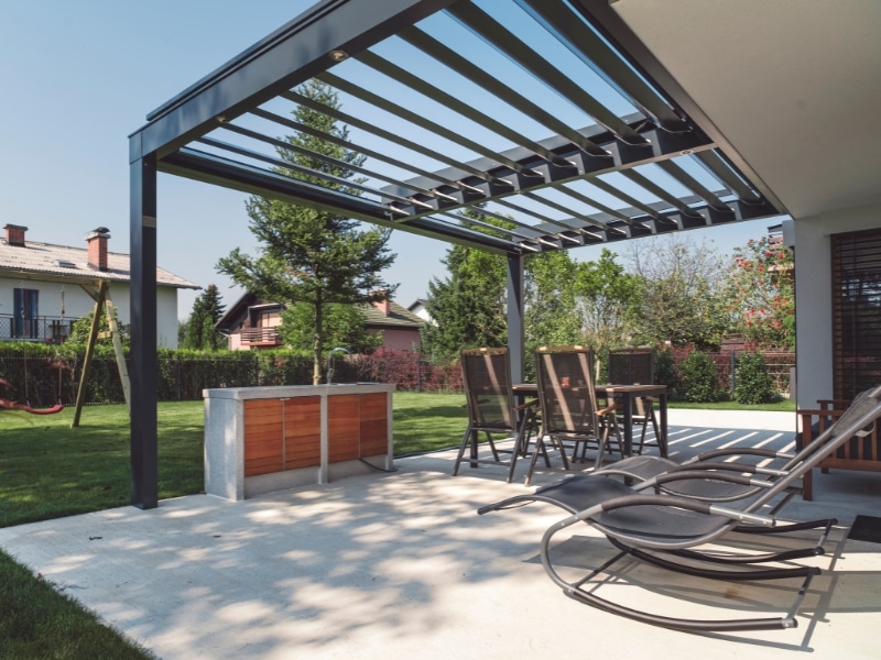 Backyard seating area under a steel pergola with open roof slats.