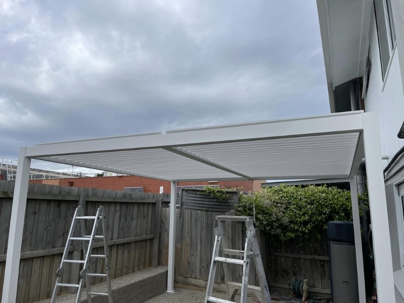 Contractors building a pergola frame in a backyard using ladders and tools.