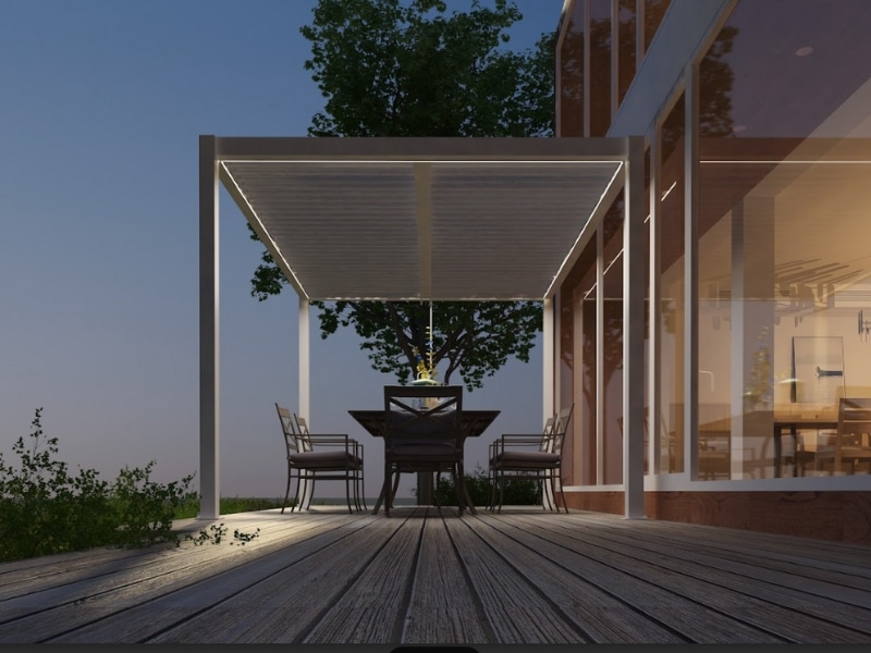 Outdoor dining area under contemporary pergola designs with LED lighting beside a modern home.