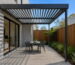 Charcoal aluminium wall-mounted louvred pergola over a compact paved courtyard beside a